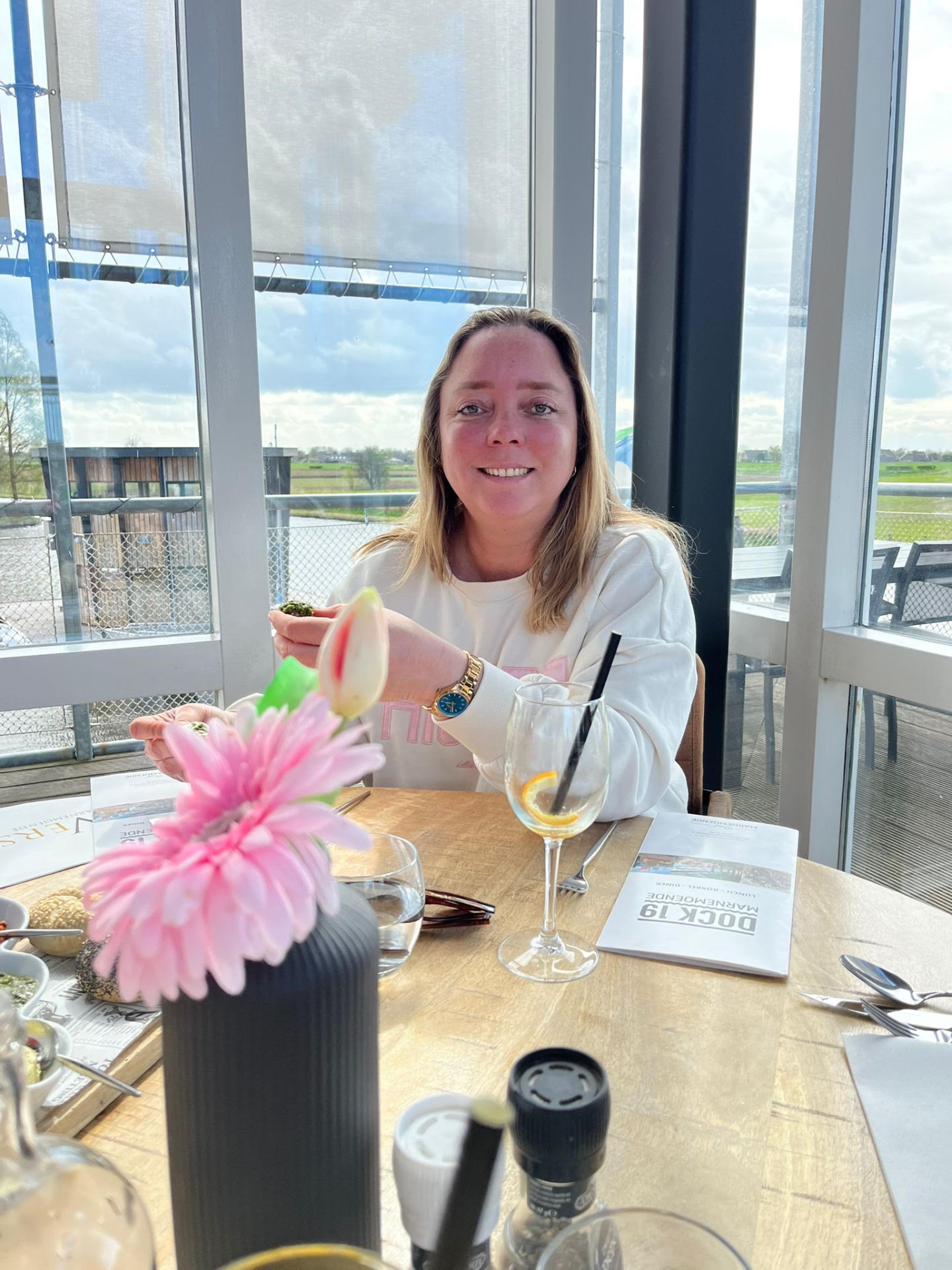 Godelieve, lachend aan tafel in een restaurant met uitzicht op het water